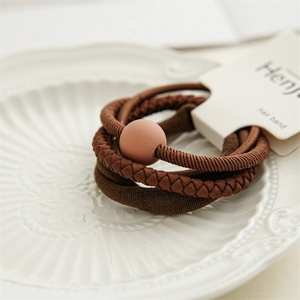 Detail of three brown elastic hair bands with a matte bead in a white ceramic dish