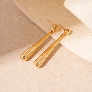 Polished gold drop earrings resting on a beige textured stone surface with natural light