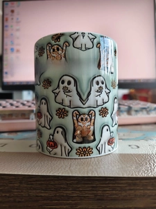 Detail of a ceramic Halloween mug with white ghosts and pumpkin patterns on a desk