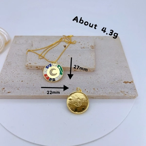 Detail of gold pendants with CZ inlay and enamel moon motif against a textured stone backdrop