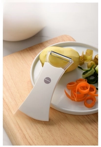 Macro detail of ergonomic white vegetable peeler with stainless steel blade on wooden board