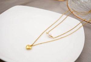 Close-up of double-layer gold heart necklace with freshwater pearl on a white ceramic plate