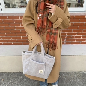 Close-up of a plush light grey lamb wool tote bag with a front pocket on a street model