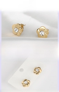 Macro detail of gold flower stud earrings with center zircon on a white satin background