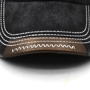 Close-up of washed gray canvas baseball cap brim with brown leather patch and zigzag stitching