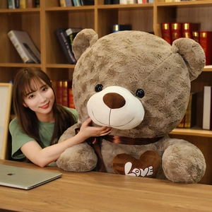 Detailed view of giant plush teddy bear with a heart Love embroidery in a cozy room