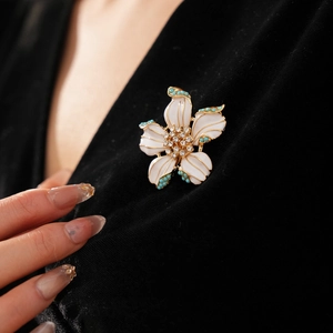 Détail d'une broche fleur vintage en émail blanc avec bordure dorée sur velours noir