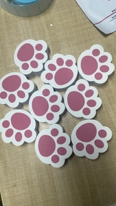 Detail view of cat paw shaped cleaning sponges in pink and white on a wood surface
