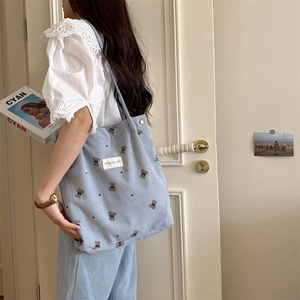 Light blue corduroy tote bag with bear embroidery shown in a side-view lifestyle shot