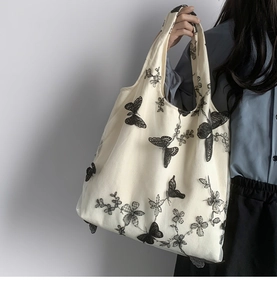 Dettaglio di ricami floreali e farfalla 3D nera su borsa tote in tela color crema