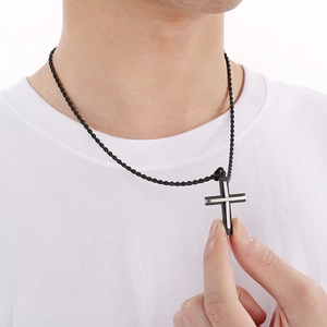Close-up of men's cross necklace with black and silver pendant on woven chain