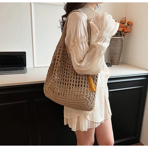 Detail of light brown woven tote bag with fringe tassels styled on a female model