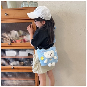 Detail of light blue plush bear crossbody bag worn by a child in a home setting