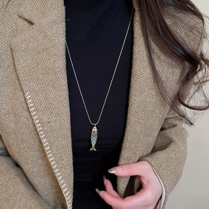 Detail view of a vintage fish pendant with blue scales on a golden bead chain