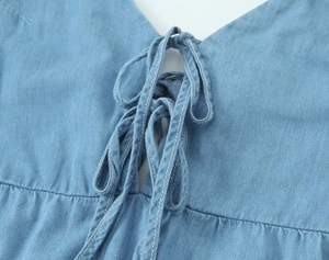 Détail d'une robe midi en denim bleu clair avec un décolleté en V à lacets