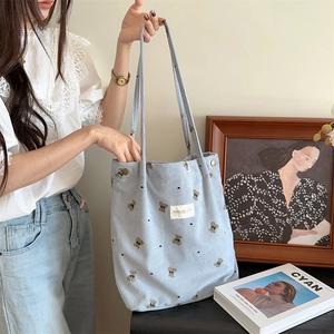 Detailed close-up of light blue corduroy tote bag with bear print and metal snap button
