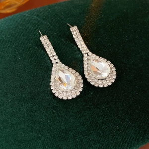 Detail of silver water-drop earrings with pavé crystals on a green velvet mat