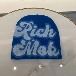 Close-up of blue knitted beanie featuring light blue Rich Mob embroidery text detail