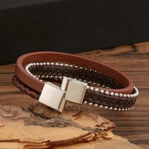 Close-up of brown braided leather bracelet with metal beads on natural tree bark texture