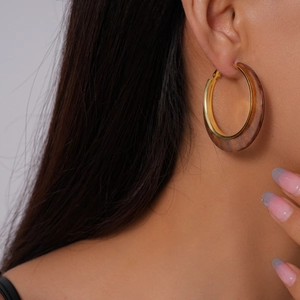 Close-up of golden hoop earrings with dark wood texture on a model's ear