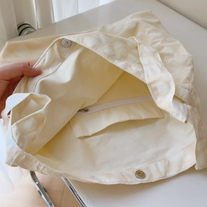 Detail of off-white canvas tote showing magnetic closure, zip pocket and textured dots