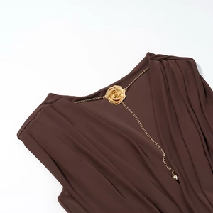 Détail d'une robe marron sans manches avec une chaîne dorée ornée d'une rose métallique