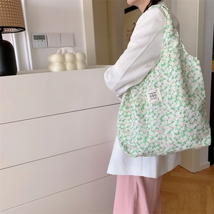 Dettaglio ravvicinato della borsa in tela a fiori verdi e rosa con etichetta tessuta