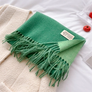 Close-up of a soft green knitted scarf with decorative tassels and brand label