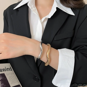 Close-up of gold and silver irregular wavy bangles styled with professional business attire