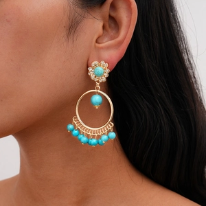 Close-up of bohemian gold hoop earrings with blue turquoise beads and floral tassels
