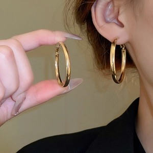 Close-up of a large gold geometric hoop earring worn by a model to show texture and size