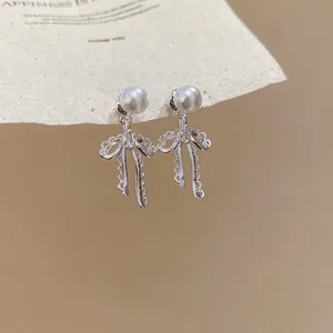 Elegant silver bow earrings with zircon and square pearl pendant on warm background