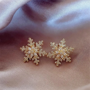 Detailed close-up of gold snowflake stud earrings with sparkling zircon on silk fabric
