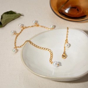 Detail of 18K gold stainless steel Cuban anklet with iridescent pearls on a ceramic dish
