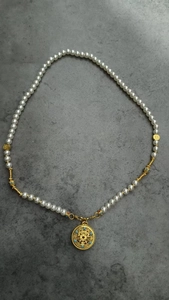 Detail showing white pearl necklace with gold hollow circular pendant and blue accents