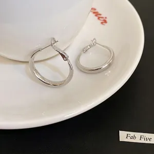 Boucles d'oreilles créoles argentées minimalistes au fini poli sur un plateau blanc