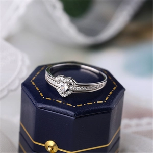 Macro shot of silver heart-shaped diamond ring on navy blue velvet jewelry box