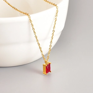 Detailed macro shot of rectangular ruby pendant on golden chain over ceramic bowl