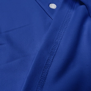 Close-up of royal blue piqué polo shirt fabric texture with a white button and stitching
