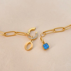 Detail van een gouden titanium stalen armband met een O-hanger en een blauwe edelsteen.