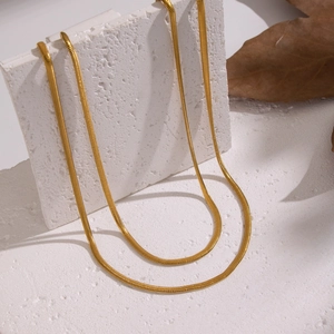 Detail einer goldenen zweilagigen Schlangenkette auf einem weißen strukturierten Stein