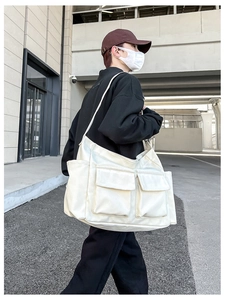 Detailed view of beige canvas messenger bag with large front pockets on a model
