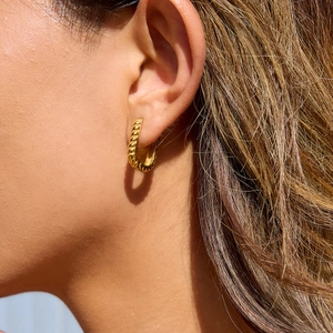 Close-up of golden U-shaped twisted earrings featuring polished metallic texture on a model