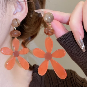 Detail of large orange resin flower tassel earrings with marble bead on model ear