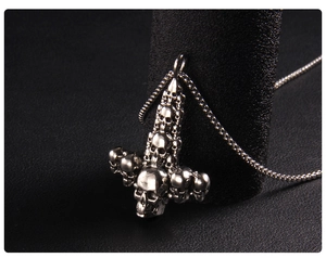 Close-up of silver punk skull and inverted cross pendant on a dark pedestal