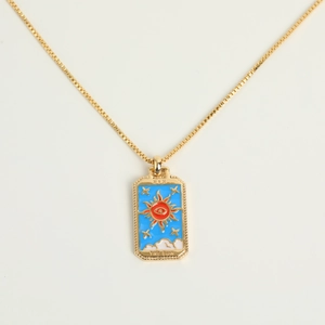 Macro detail of gold tarot sun necklace with blue enamel and evil eye center