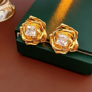 Gros plan de boucles d'oreilles fleur dorées avec cristal carré sur un écrin vert