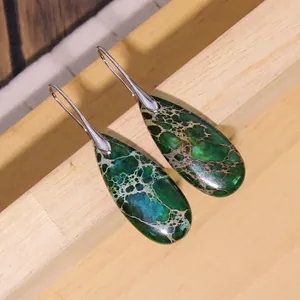 Macro view of teardrop imperial stone earrings with green marbled texture on wood