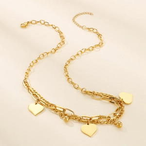 Detail of layered gold necklace featuring a heart pendant and round beads on soft beige surface