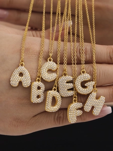Macro detail of 18k gold plated letter pendants A-H with sparkling cubic zirconia inlay